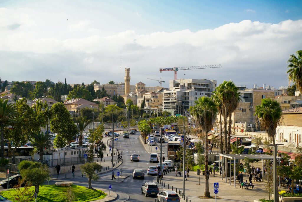 View of Jerusalem streets with historic buildings and palm trees under a clear blue sky.