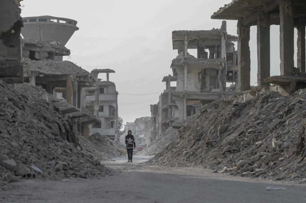 A solitary figure walks through the devastated ruins of Damascus, Syria, highlighting the aftermath of conflict.