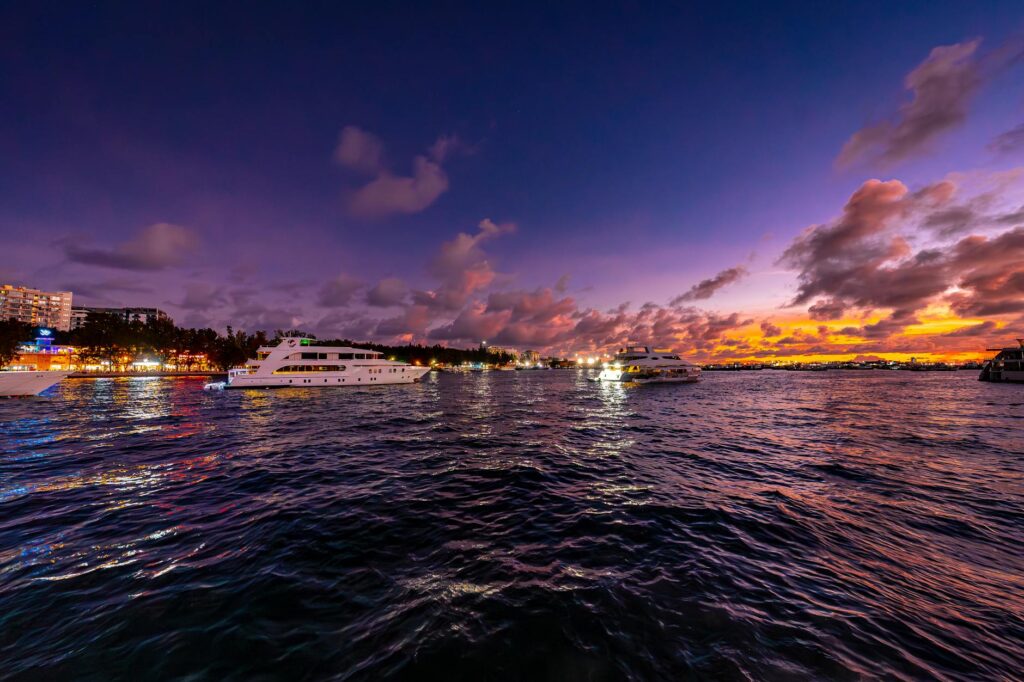 An elegant yacht anchored in Maldives marina during a vibrant sunset with colorful skies.