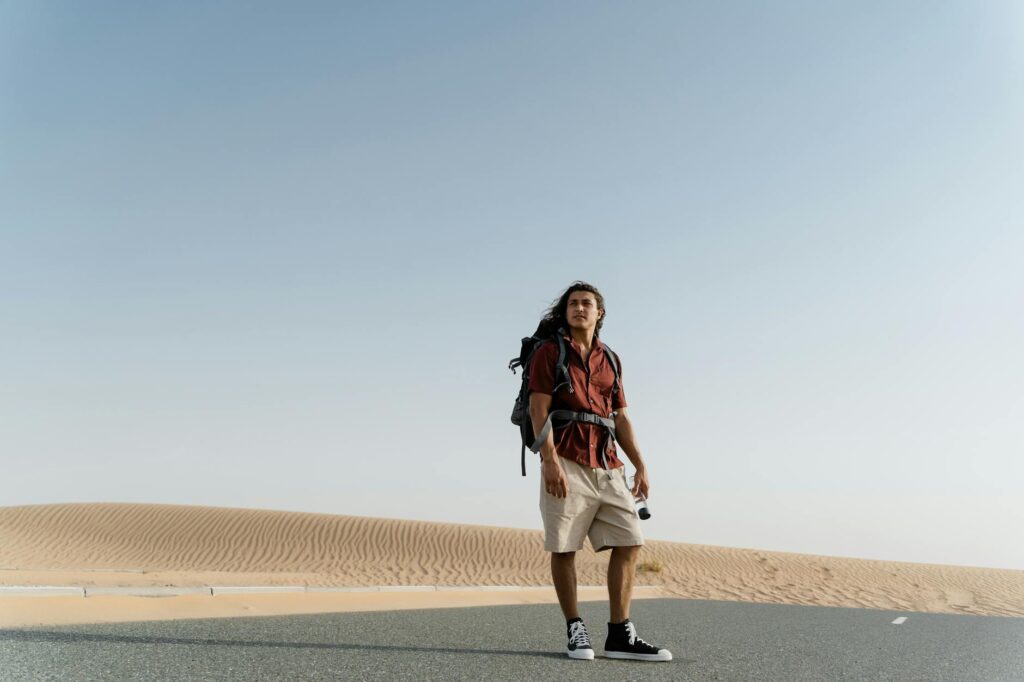 Man on a desert road enjoying outdoor adventure with a backpack during the day.