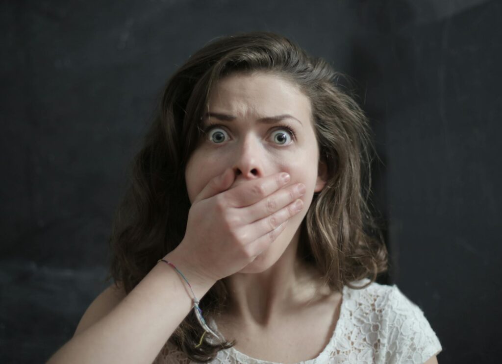 Close-up of a woman with a shocked expression, covering her mouth with her hand. Emotional and intense moment.