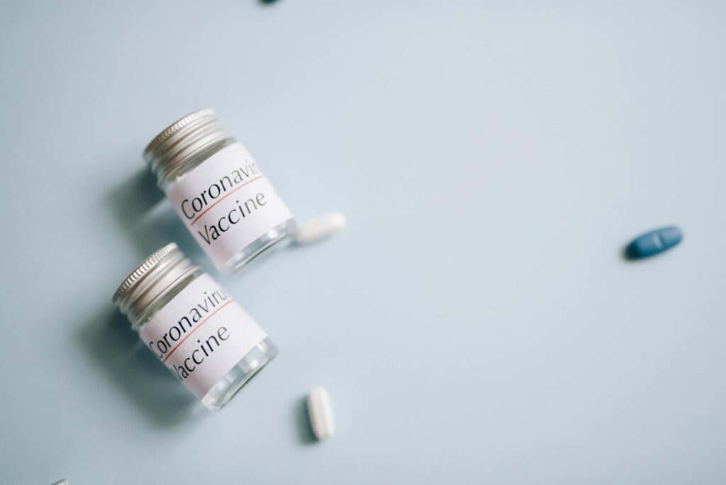 Close-up of coronavirus vaccine vials with scattered pills on a blue background, symbolizing healthcare efforts.