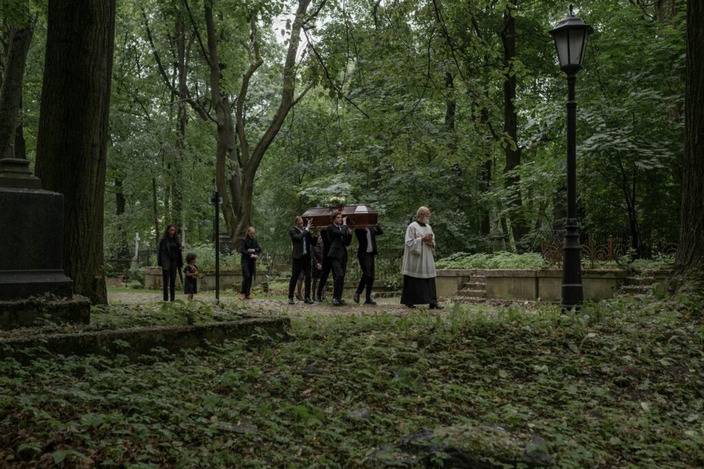 A funeral procession with mourners carrying a coffin through a serene forest cemetery.