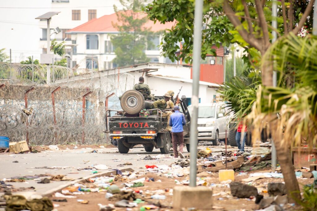 Military personnel patrol a city street with debris in an urban conflict setting.