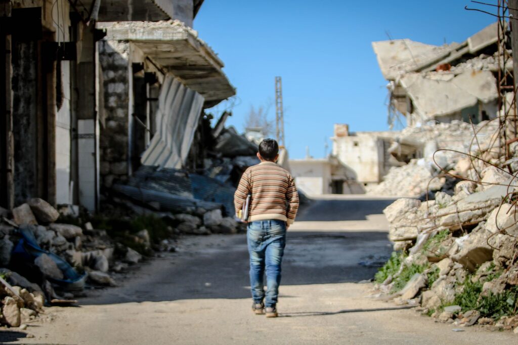 A young boy walks through the demolished streets of Idlib, Syria, amidst the rubble and destruction.