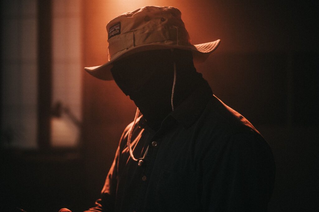 Silhouette of a person wearing a hat with dramatic lighting and shadow effects creating a mysterious atmosphere.