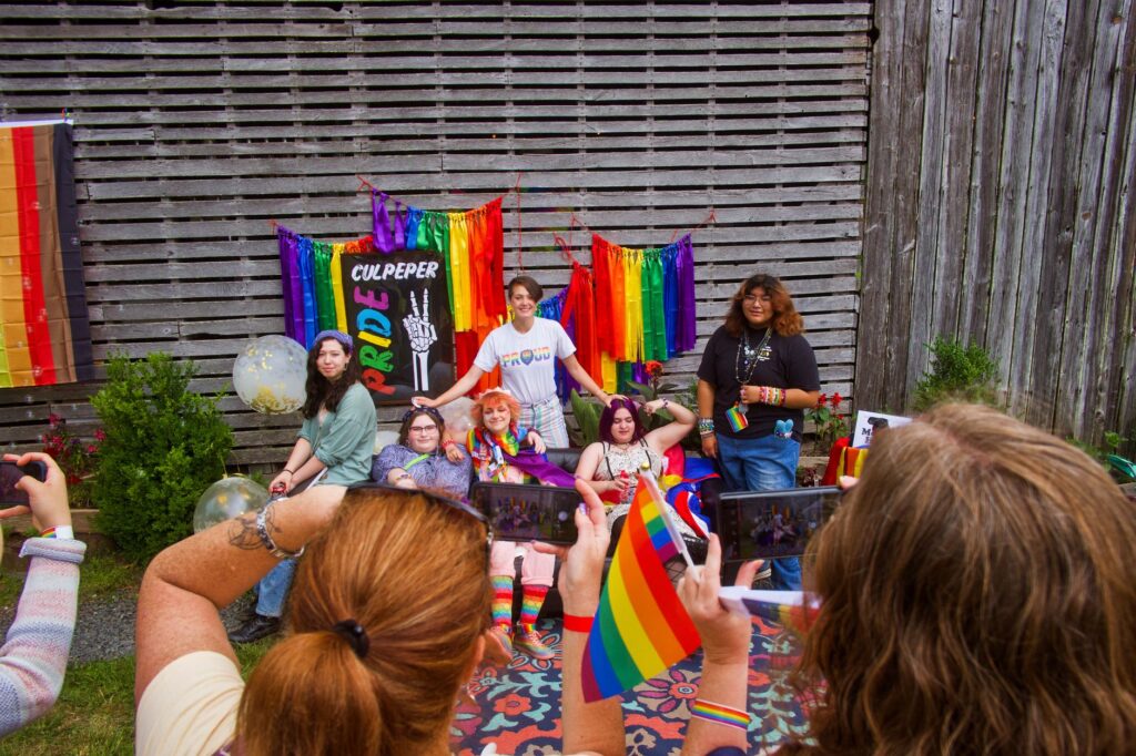 Group of diverse individuals celebrate Pride with colorful flags and joyful smiles outdoors.