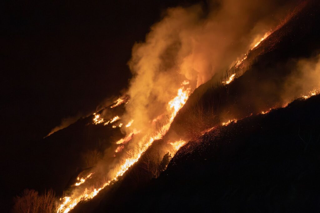 Intense blaze sweeping through a steep mountain forest at night, highlighting wildfire impact.