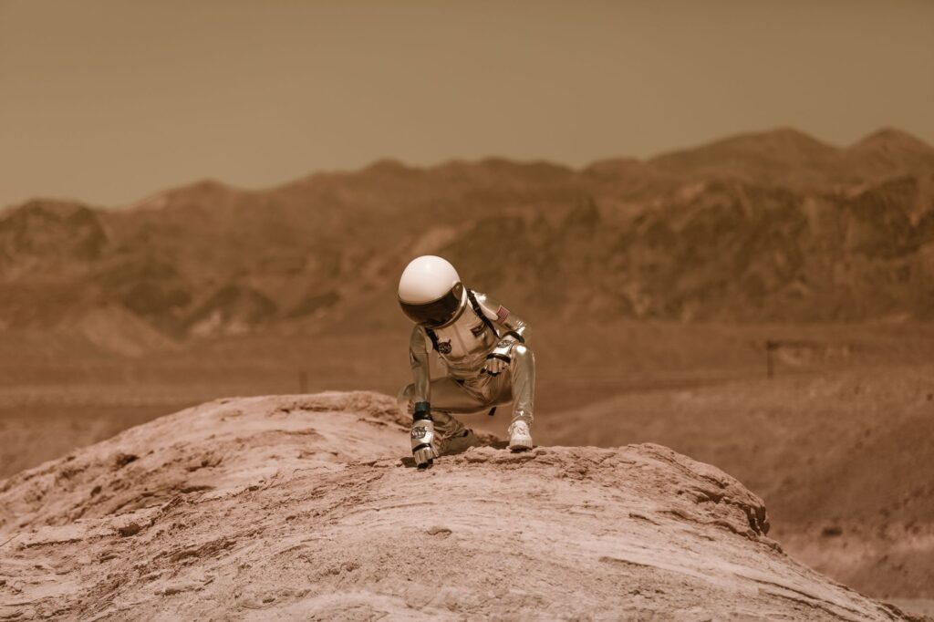 An astronaut in a space suit exploring a Mars-like desert environment, crouching on a rocky surface.