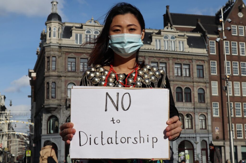 Person holding a sign saying 'No to Dictatorship' during a protest in an urban setting.