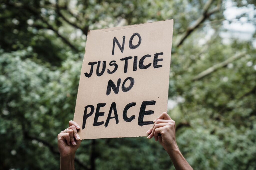 Close-up of a protest sign reading 'No Justice No Peace' held up outdoors. Focus on activism.