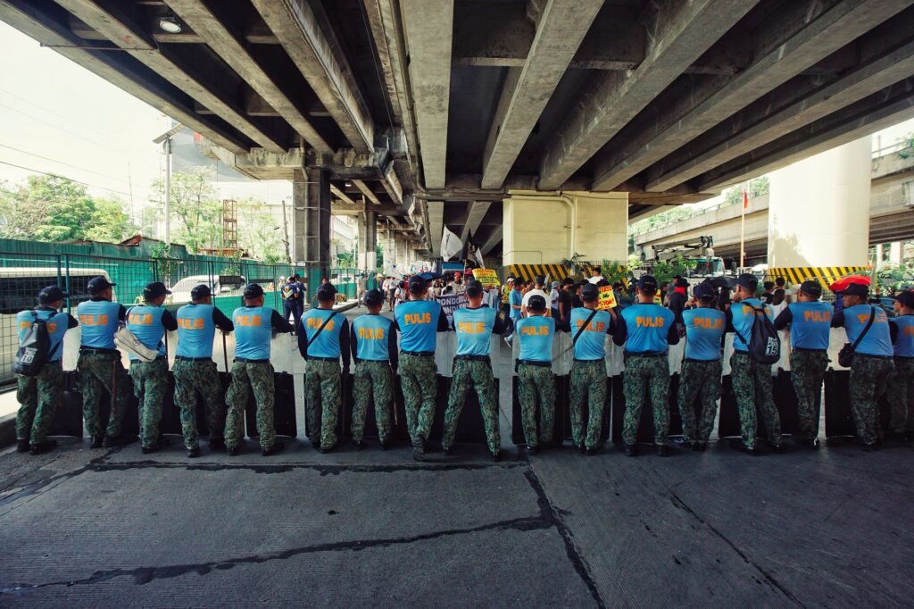 A line of police officers in blue uniforms standing under a bridge during a daylight operation.
