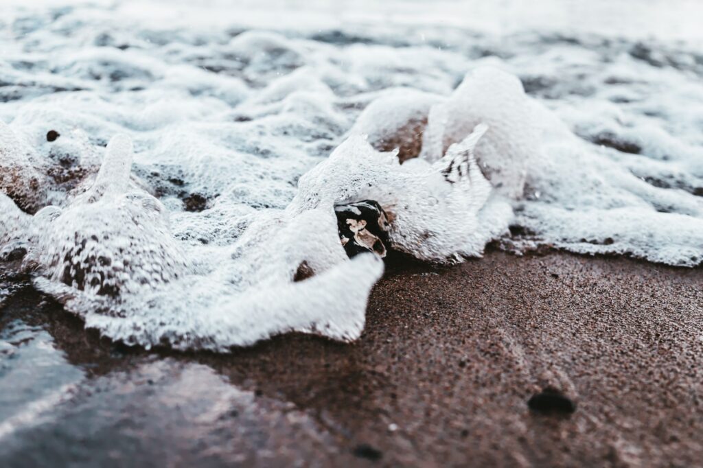 A detailed view of sea foam gently covering the sandy beach, capturing the beauty of ocean waves.