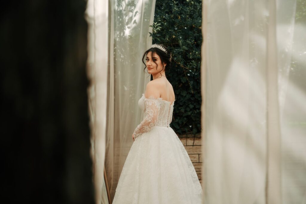 A beautiful bride in a lace gown and tiara stands outdoors, creating a dreamy wedding scene.