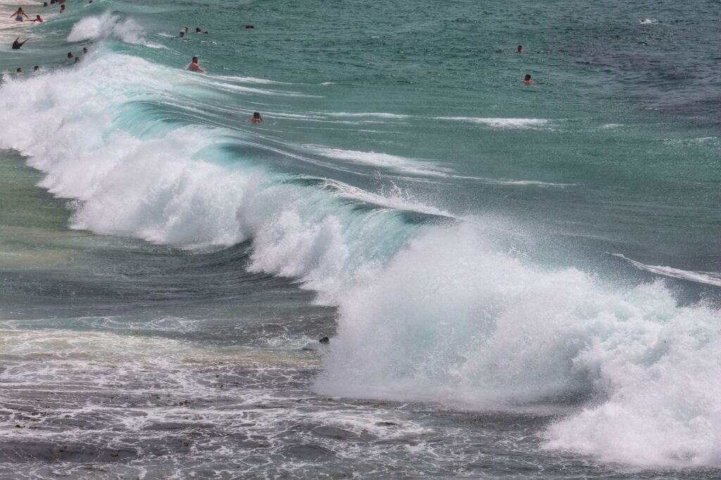 Dynamic ocean waves crashing on a beach with numerous swimmers enjoying the water.