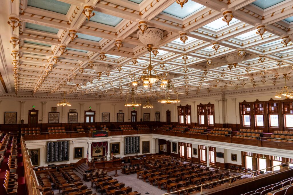 Interior view of the ornate Texas Capitol House Chamber in Austin with decorative ceiling and empty seats.