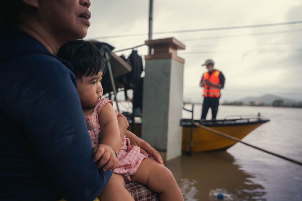 A mother holds her child amid floodwaters in Phú Yên, Vietnam, showcasing resilience and community support.