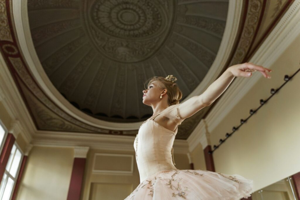 Graceful ballerina in a tutu posing elegantly under a decorative ceiling in a classical room.