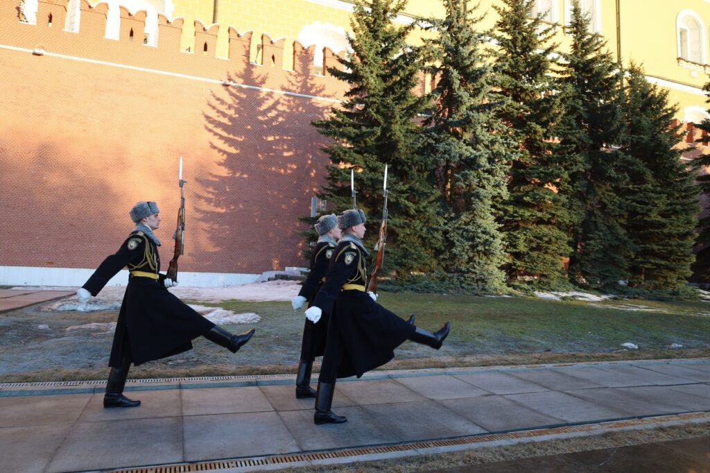 Ceremonial guards march outside the Kremlin walls in Moscow on a bright day.
