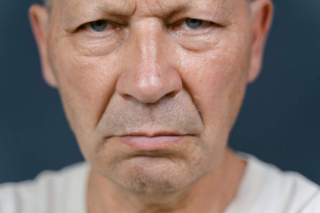 A detailed close-up of a senior man's face showing a serious expression, enhancing the texture of aged skin.
