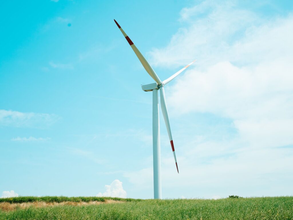A wind turbine stands tall against a clear blue sky on a grassy field, symbolizing renewable energy.