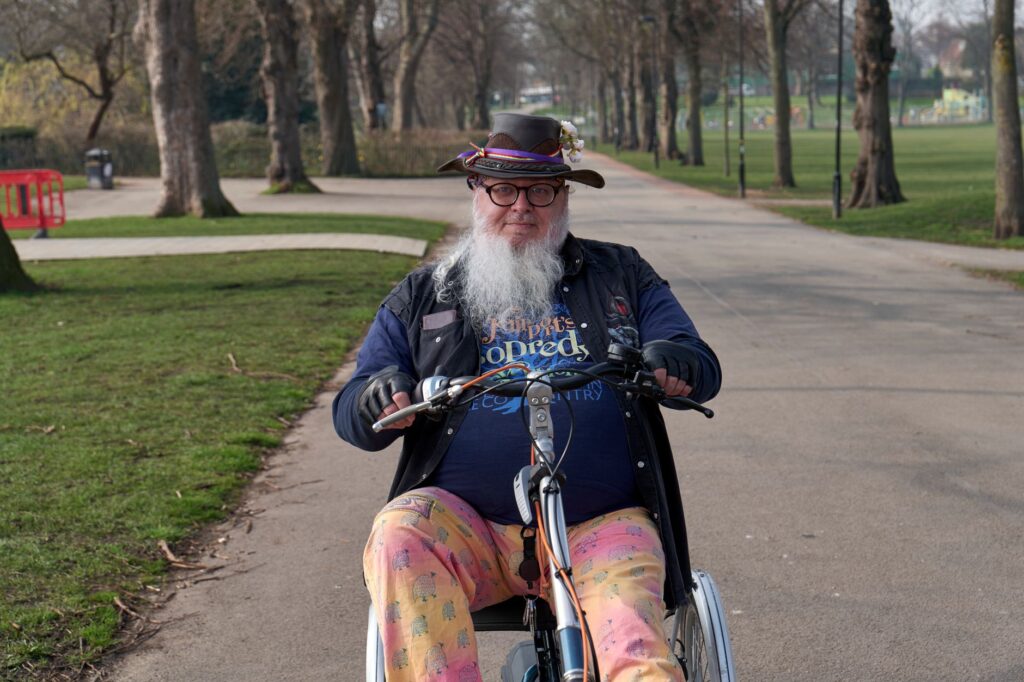 An elderly man with a hat and beard rides a specialized bike in a serene park setting.